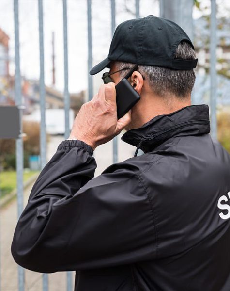 Confident mature security guard talking on mobile phone in front of gate