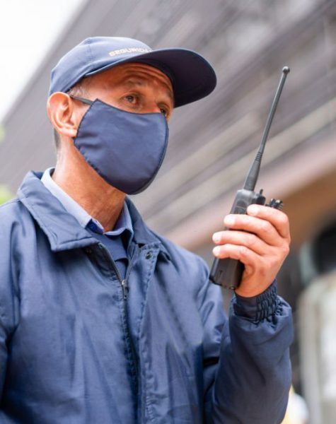 Portrait of a Latin American Security guard outdoors wearing a facemask while working at a shopping mall during the COVID-19 pandemic and using a walkie-talkie