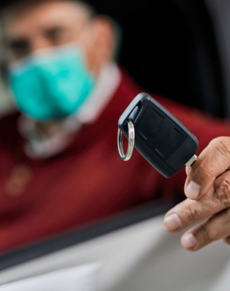 Close-up of a man holding keys of his new car while wearing face mask during coronavirus epidemic.